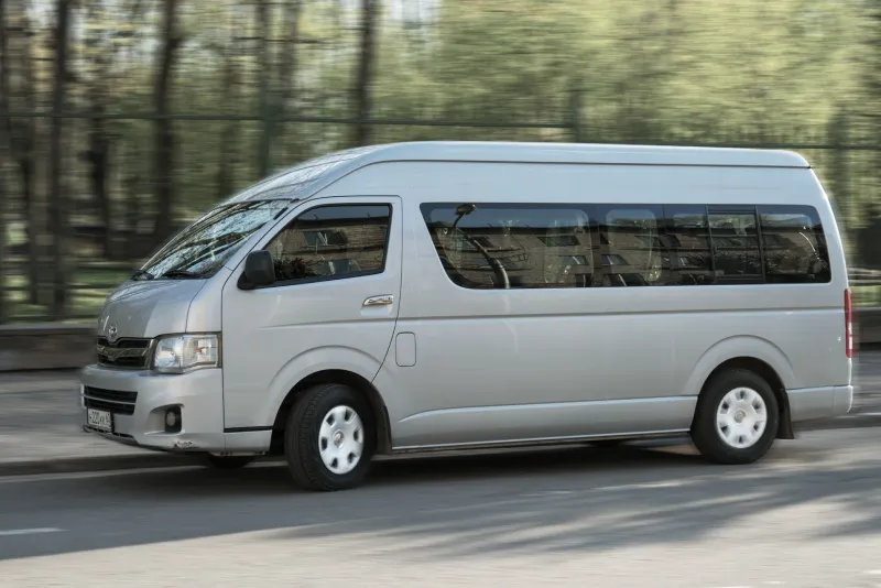 街中の道を走行するシルバーの送迎用マイクロバス。