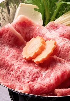 鮮やかな赤身にきめ細やかな白い霜降りがのった、大判の和牛。春菊や豆腐、花形にカットされた人参とともに、鍋に美しく盛り付けられています。