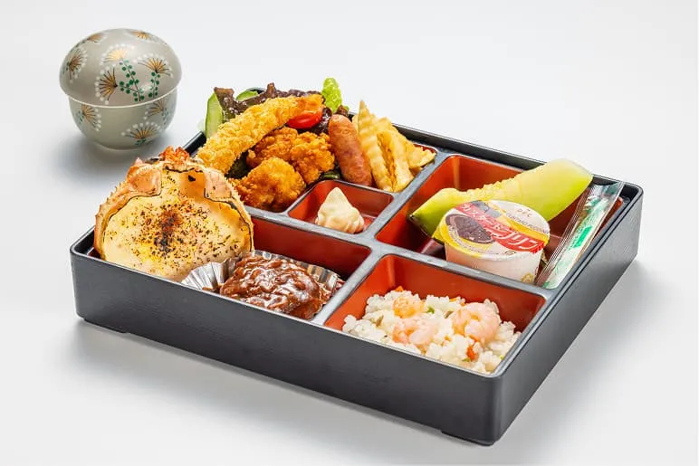 黒いお弁当箱に、お子様に人気のメニューが贅沢に並んでいます。大きなエビフライ、唐揚げ、ハンバーグ、ポテトフライに加え、カニの甲羅に入ったグラタンやエビピラフがセットになっています。