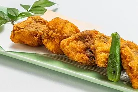 薄緑色の長皿に盛り付けられた、こんがりときつね色に揚がった河豚の唐揚げ。