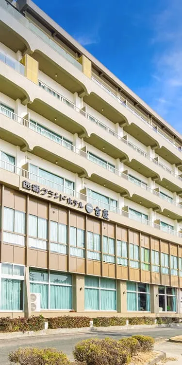 青い空とヤシの木に囲まれた、西浦グランドホテル吉慶の外観全景。