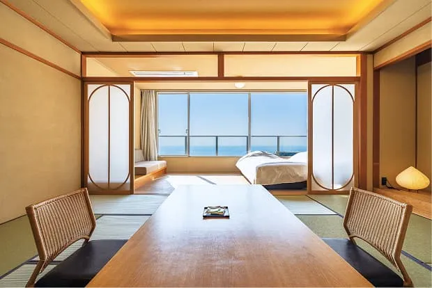 手前に座卓を配した畳敷きの和室、その奥にベッドとソファを設えたモダンな広縁。繊細な木枠の仕切り越しに、窓の外に広がる青い三河湾を一望できる開放的な客室。