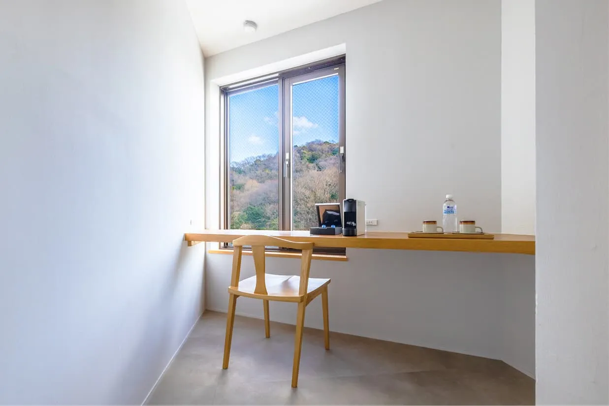 客室『wan〜湾〜』のワークデスク。窓に面した長い木製カウンターに、シンプルな一脚の椅子が置かれています。