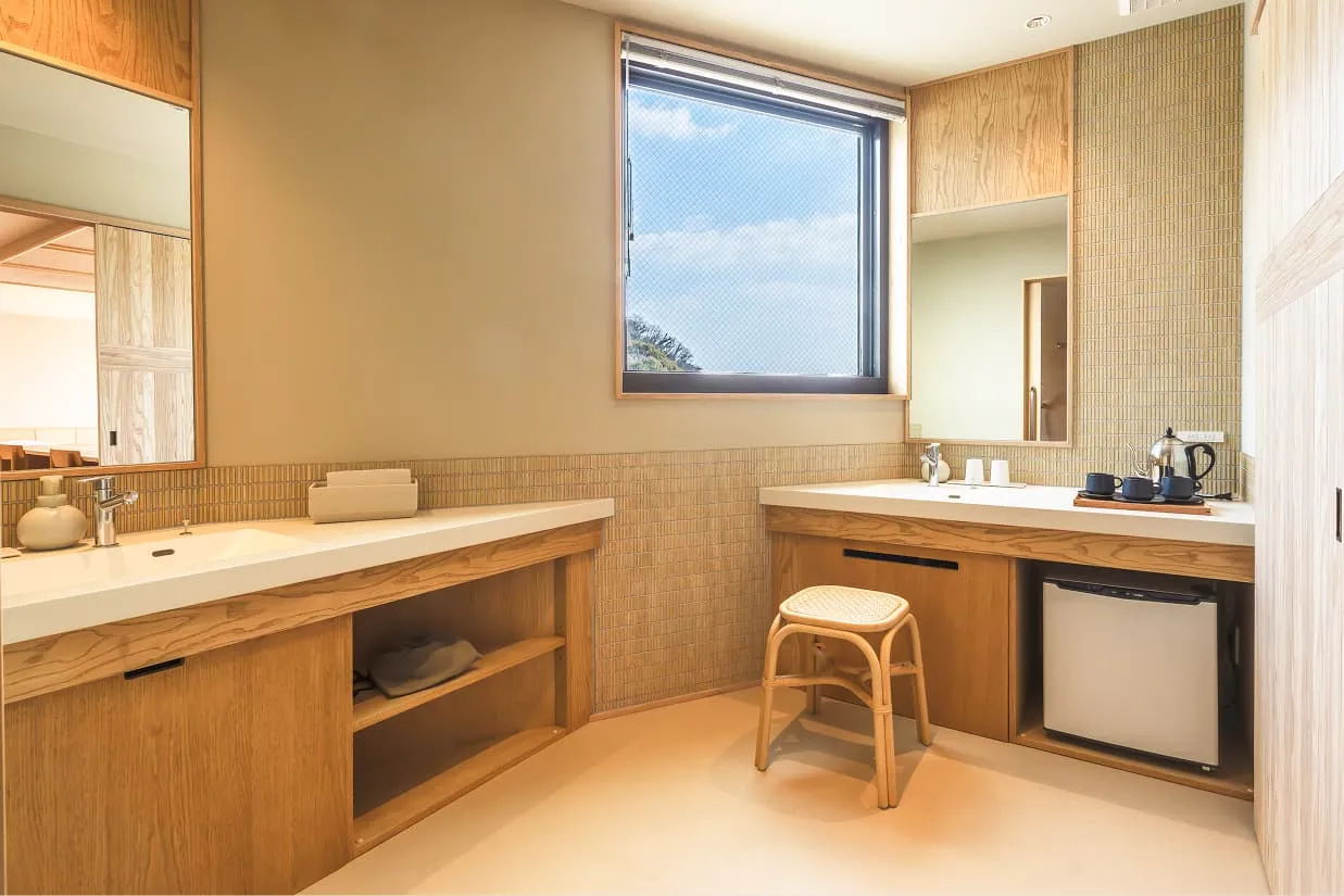 ユニバーサルデザインに配慮した、広々とした洗面スペース。木製のカウンターがL字型に配置され、左側に洗面台、右側にミニバーと2つ目のシンクがあります。車椅子のまま利用できるよう、カウンター下は足元がオープンな設計になっており、中央には補助用の丸椅子も用意されています。