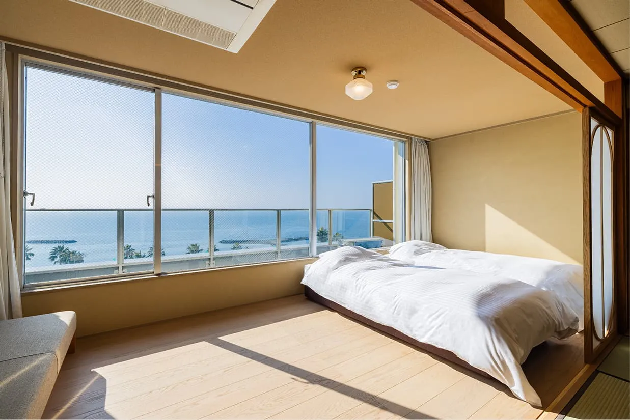 窓際に配置されたツインベッド。大きな窓からは遮るもののない青い海と空が広がり、室内には明るい陽光が差し込んでいます。
