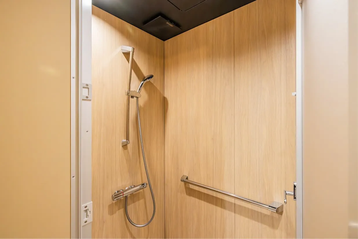 明るい木目調の壁面が印象的なシャワーブース。高さ調節が可能なスライドバー付きのハンドシャワーと、横に長い手すりが設置されています。