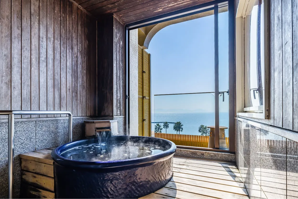 海を望むテラスに設えられた、深みのある藍色の陶器製露天風呂。湯口からは清らかなお湯が注がれ、水面からは柔らかな湯気が立ち上っています。