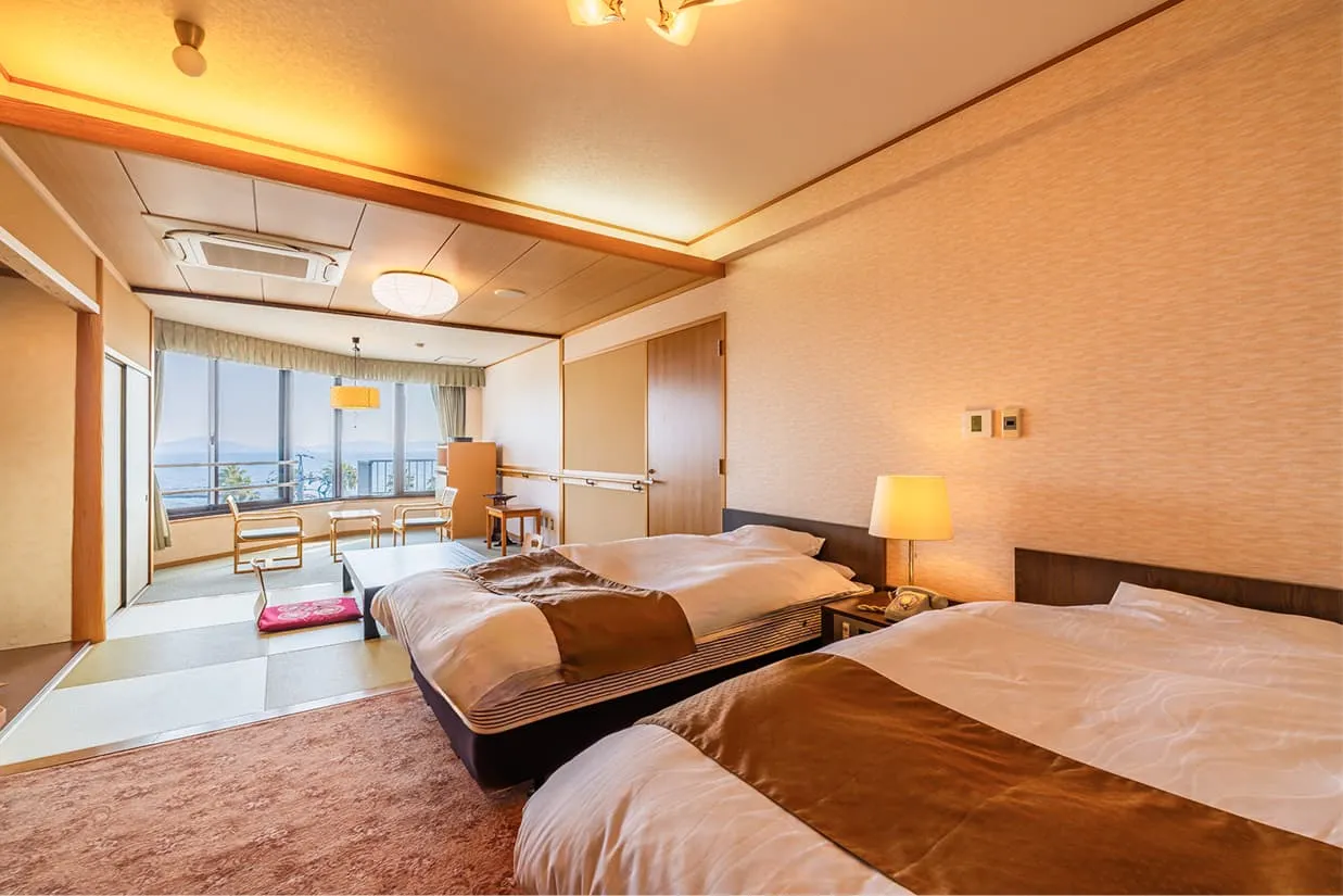海を一望できる大きな窓がある、広々としたバリアフリー和洋室。手前にはツインベッドが置かれたカーペット敷きの洋室エリアがあり、奥には座椅子や座卓を備えた琉球畳風の和室スペースが続いています。