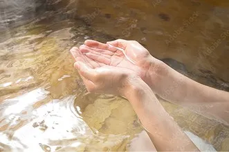 両手でそっと温泉をすくい上げている様子。