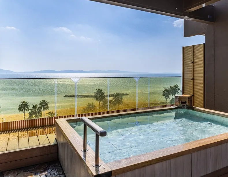 木のぬくもりがある落ち着いた浴室。大きく開かれた窓の向こうには、穏やかな波が光る青い三河湾と、遠くに連なる山々のパノラマが広がっています。