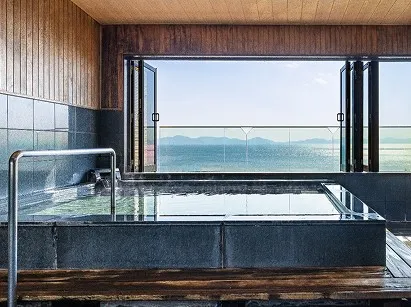 木枠の露天風呂。透明な湯の向こうには、透明な仕切り越しにヤシの木が並ぶ砂浜と、キラキラと輝く穏やかな三河湾が水平線まで見渡せます。