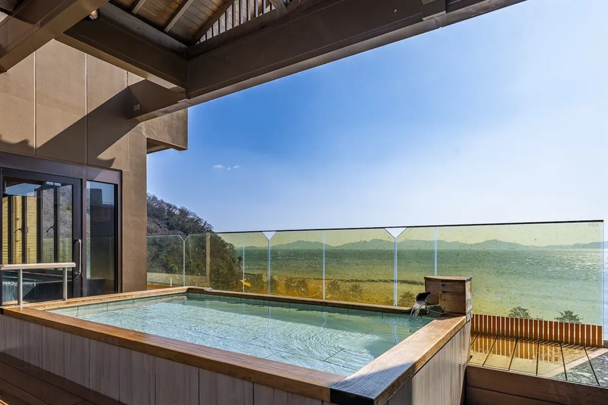 奥行きのある展望露天風呂。手前から奥へと続く木枠の湯船の先に、透明なフェンス越しに三河湾の大パノラマが広がっています。