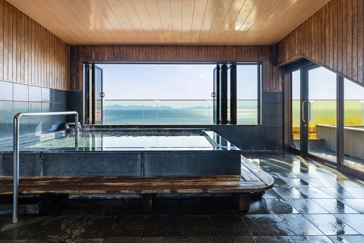 木の温もりに包まれた屋内展望風呂。正面の大きな窓は左右に開放されており、湯船に浸かりながら水平線まで続く穏やかな三河湾を、絵画のように一望できます。